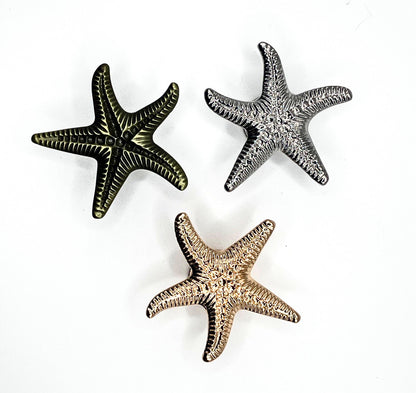 Three starfish-shaped objects in gold, silver, and bronze on a white background