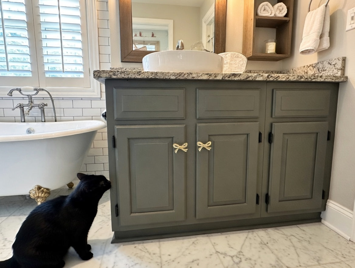 Bathroom with gray vanity, freestanding bathtub, and black cat.