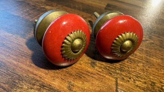 Two red ceramic door knobs with gold metallic centers on a wooden surface