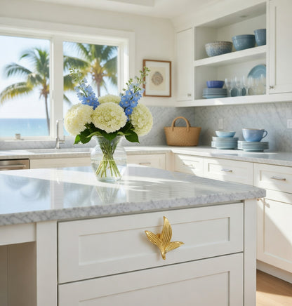 Modern kitchen with gold Sera leaf knob, marble island, floral arrangement, and ocean view