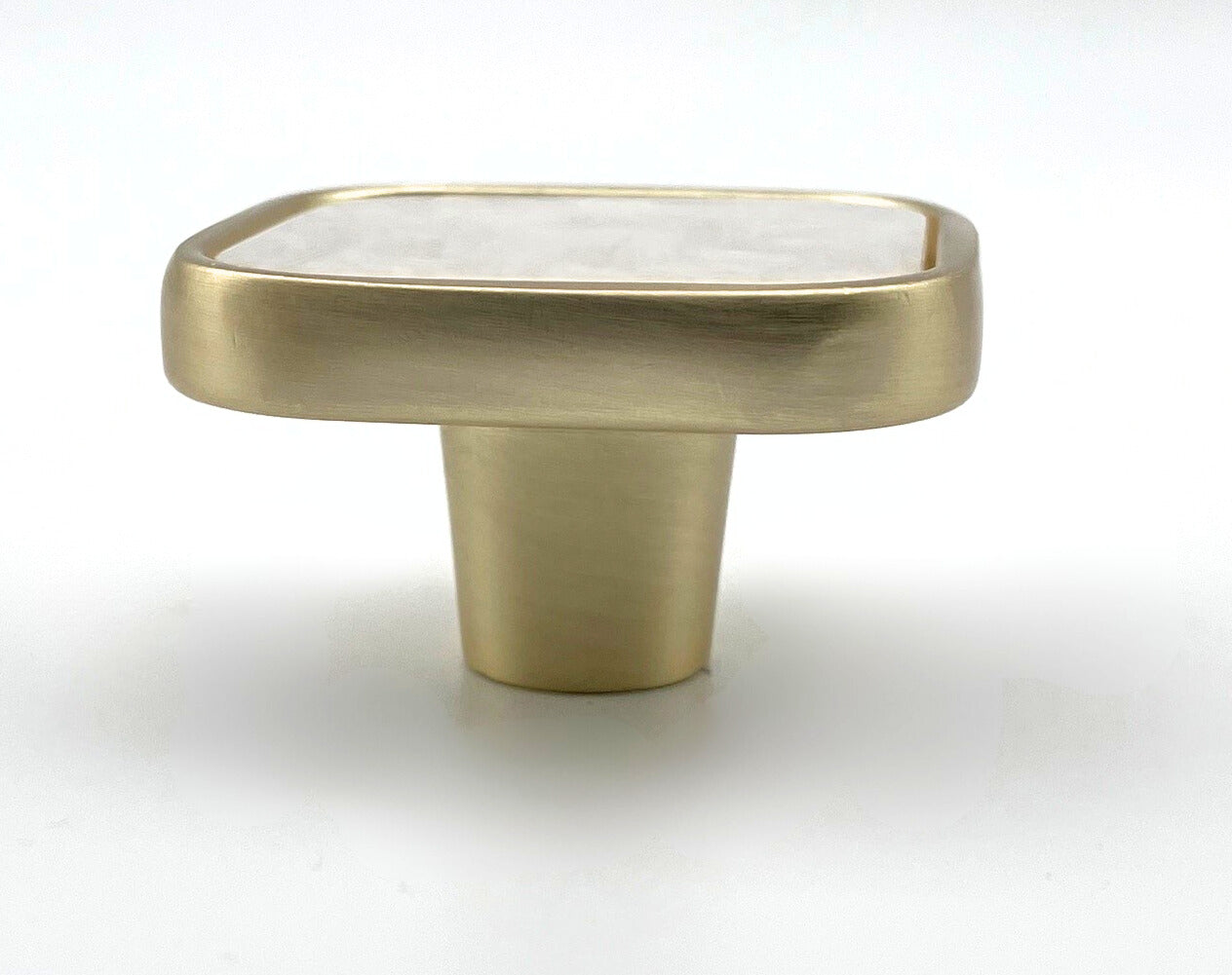 Square with rounded corners shaped knob with off-white inset and brass gold metal trim