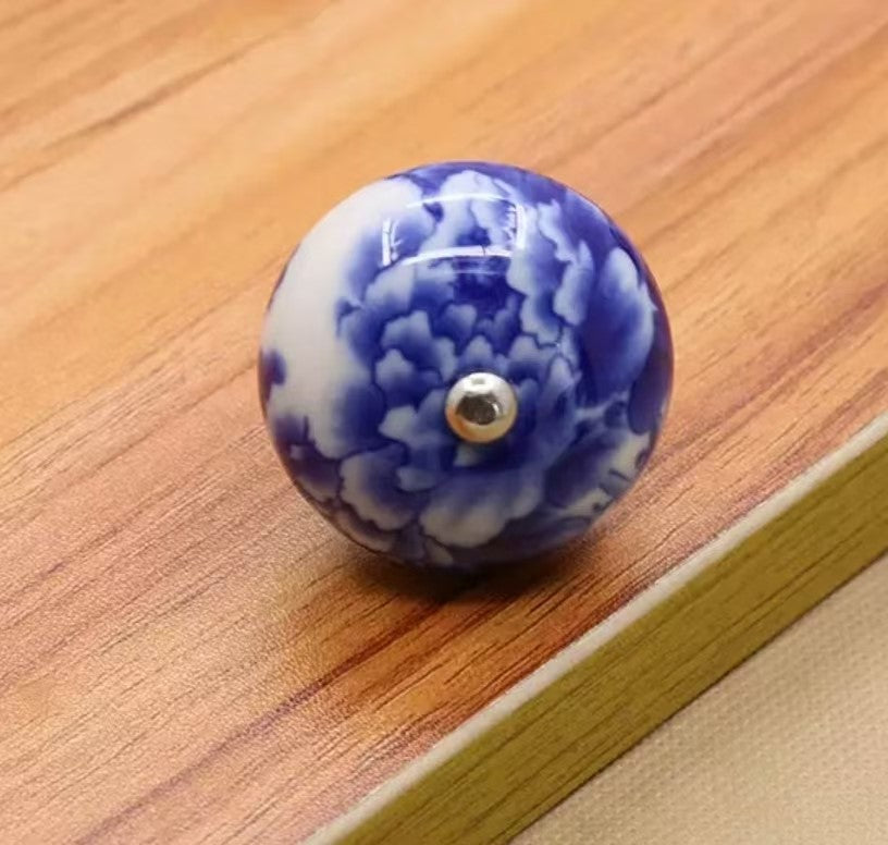 Round ceramic knob with blue floral pattern and silver trim on a cabinet
