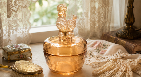 Marigold glass poodle jar styled on an antique dressing table with vintage accessories, flowers, and warm natural light.