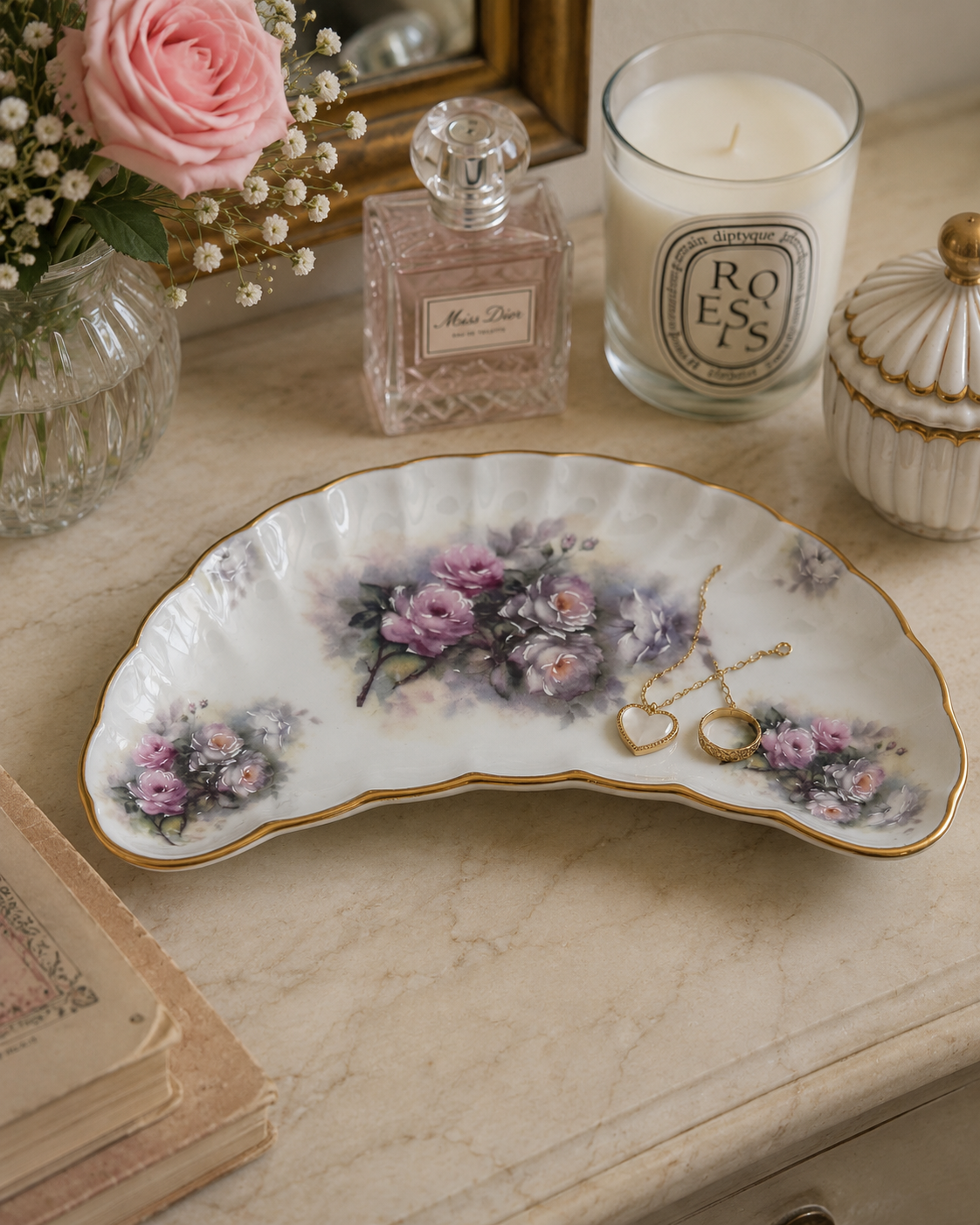 Floral crescent porcelain trinket tray displayed with jewelry and perfume on an elegant vanity table.