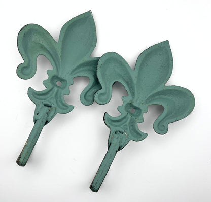 Two rear facing green fleur-de-lis wall hooks on a white background