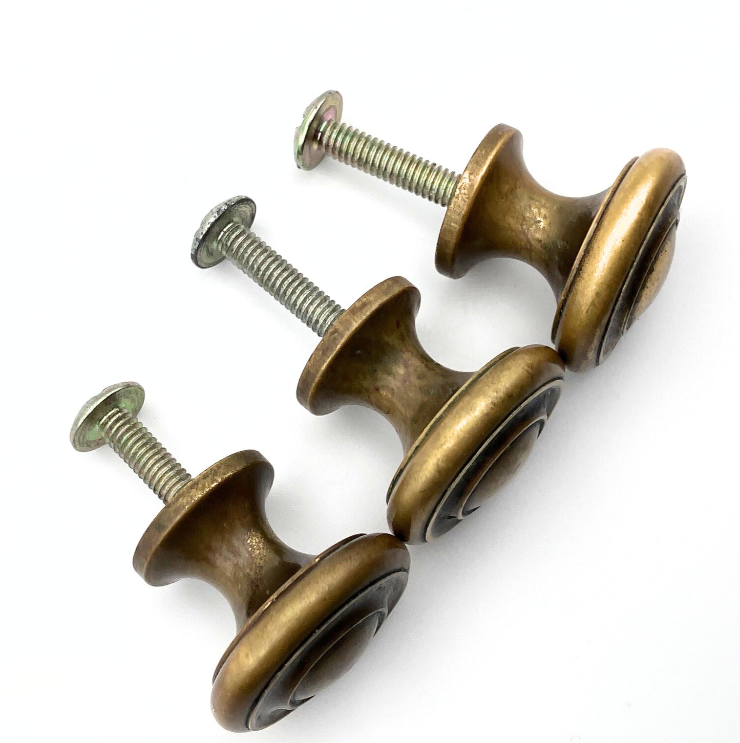 Three brass cabinet knobs with screws on a white background