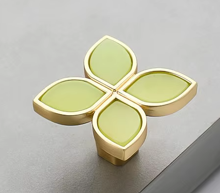 4 petal knob with each green petal surrounded in gold trim on a cabinet