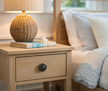 Wooden nightstand with wicker lamp and books next to a bed with striped bedding.