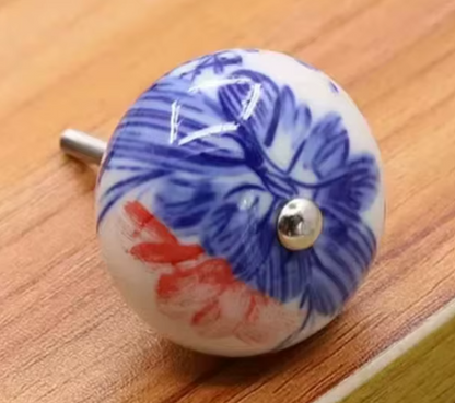 Round ceramic knob with blue and coral floral pattern and silver trim on a wooden surface