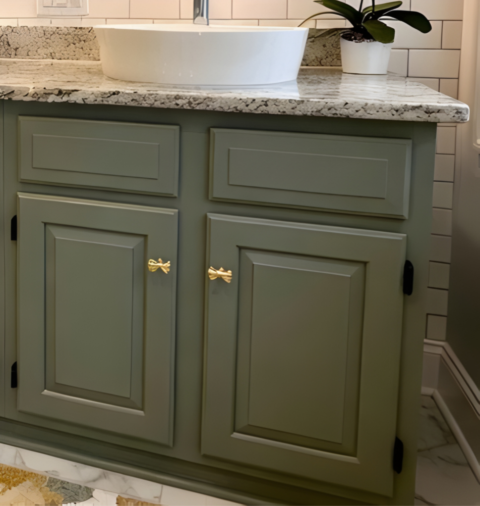 Green bathroom vanity with gold bow handles and a white sink.