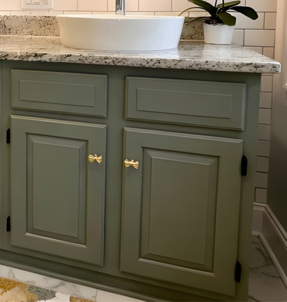 Green bathroom vanity with gold bow handles and a white sink.