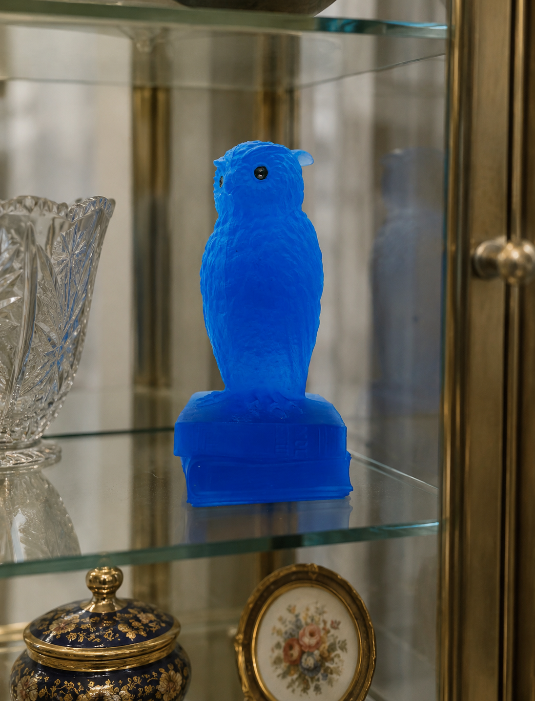 Vintage cobalt blue owl figurine displayed inside a glass curio cabinet alongside coordinating blue art glass and collectibles.