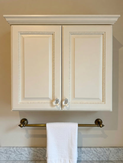 White cabinet with gold towel rack and white towel on a marble countertop.