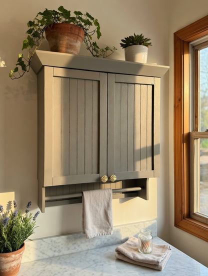 Wooden cabinet with shutters on a wall, decorated with plants and towels.