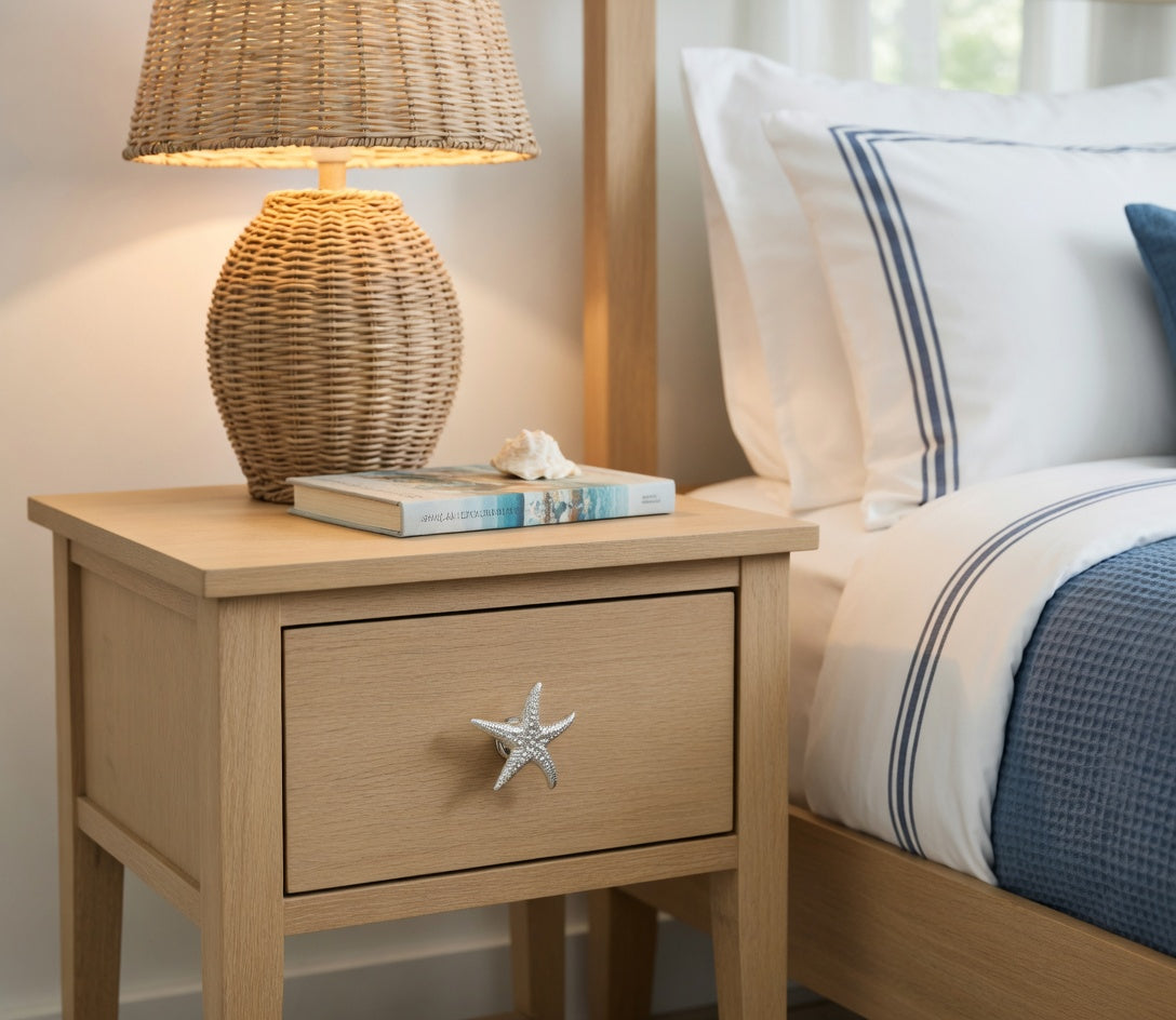 Wooden nightstand with a lamp and books next to a bed with white and blue bedding.