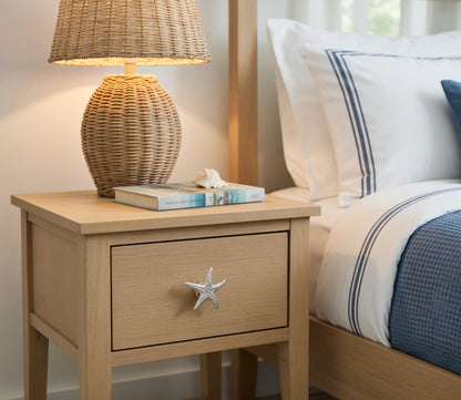 Wooden nightstand with a lamp and books next to a bed with white and blue bedding.