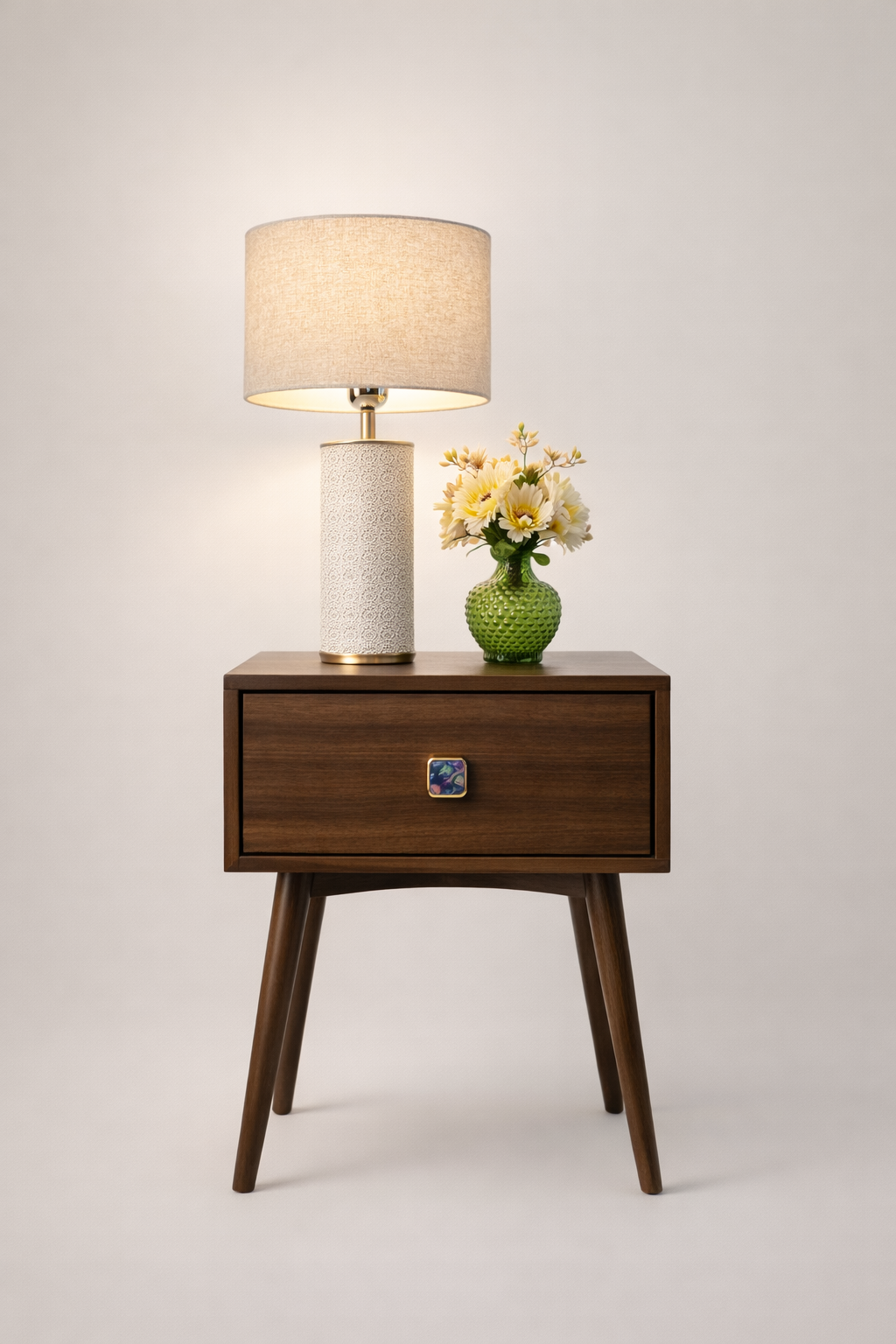 Wooden nightstand with a lamp and vase of flowers on a light gray background