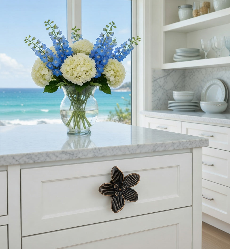 Kitchen counter with bronze flower knob, a vase of blue and white flowers, ocean view through window